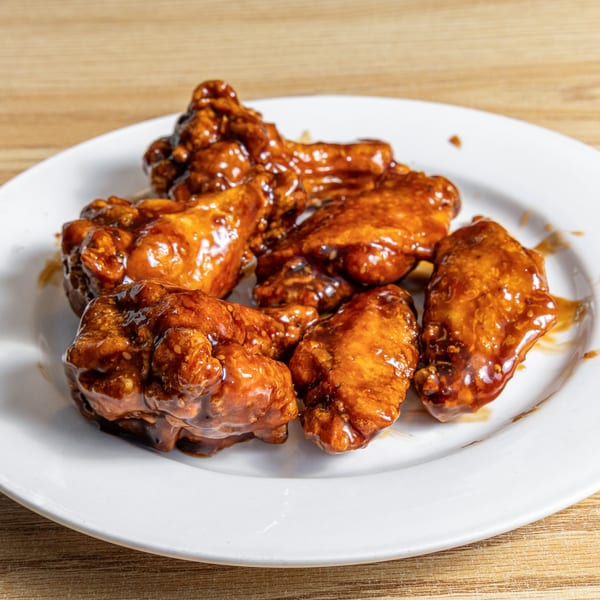 A white plate holds several pieces of chicken wings coated in a glistening, dark brown sauce.