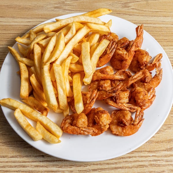A white plate holds crispy fried shrimp and golden french fries on a wooden table.