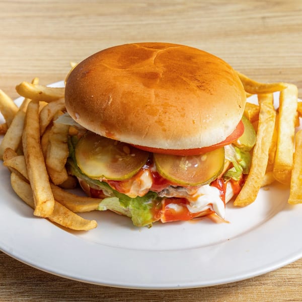 A fish burger with lettuce, tomato, pickles, and sauces, served with a side of french fries.